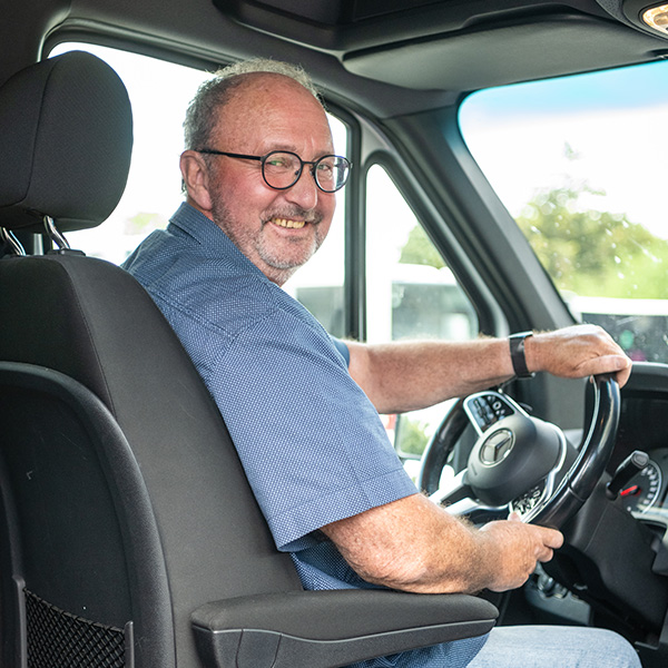 Ein Busfahrer von Verhuven sitzt lächelnd am Steuer eines Kleinbusses.