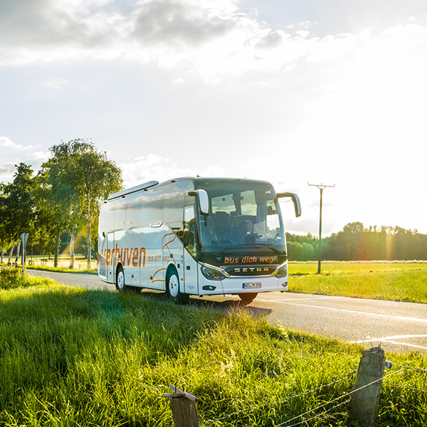 Reisebus wird von einem Busfahrer gefahren und fährt durch eine grüne Landschaft.