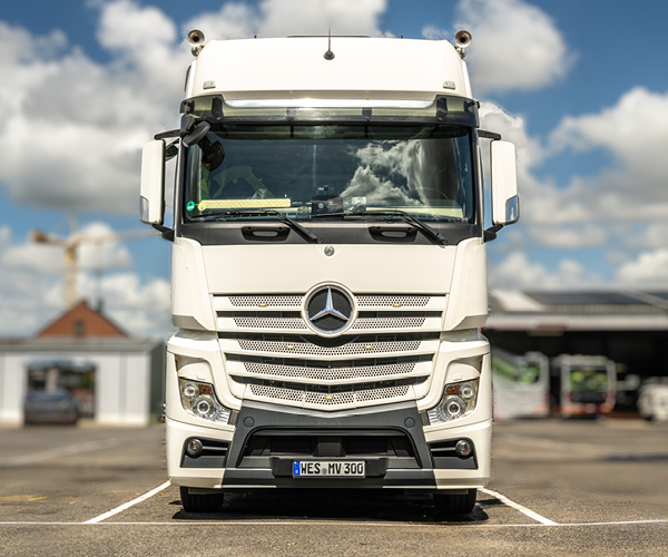 Weißer Mercedes-Lkw von Verhuven für Logistik- und Siloaufträge auf dem Betriebshof vor blauen Himmel mit Wolken.