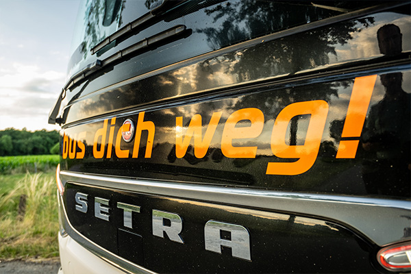 Man sieht die Vorderseite eines Setra-Reisebusses mit der Aufschrift "bus dich weg!"