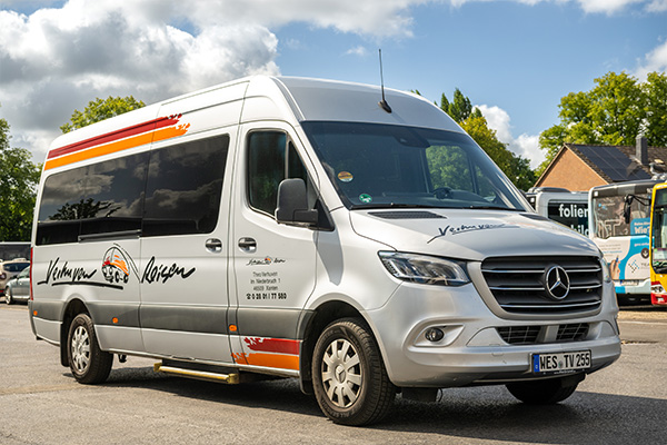 Ein silberner Mercedes Sprinter mit der Aufschrift Verhuven Reisen auf einem Betriebshof.